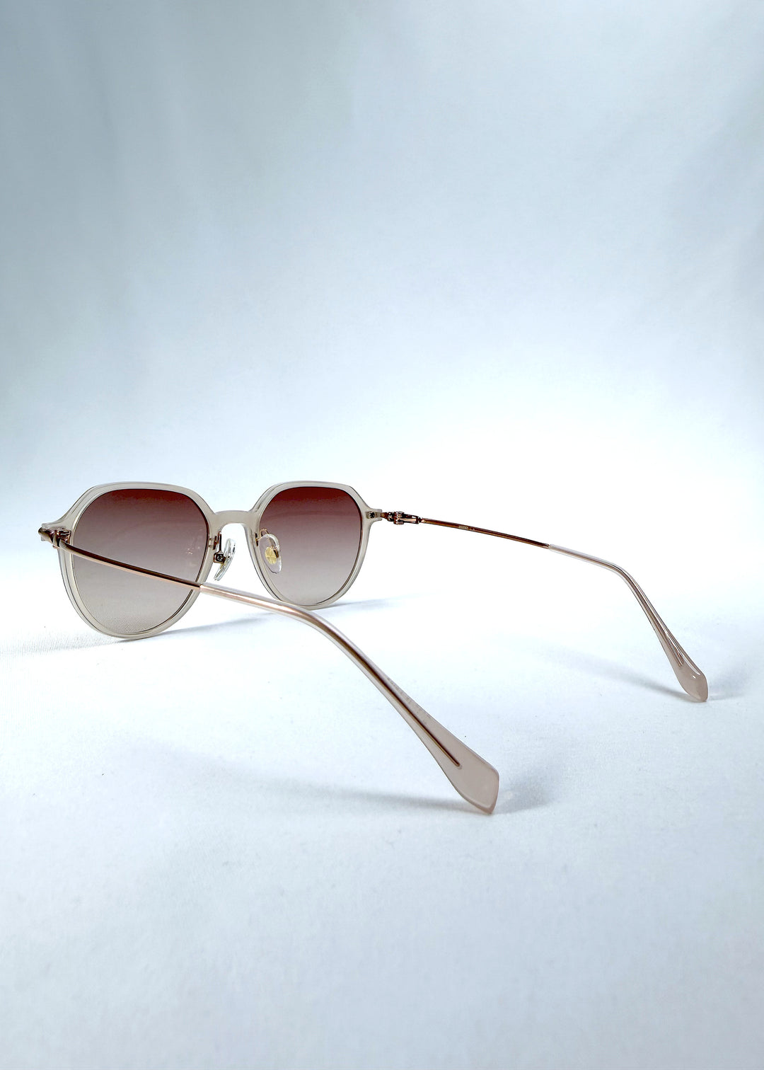 Back-angle view of AZE Vireo Arc sunglasses in Roselight, featuring a translucent ivory frame and soft rose gradient lenses, showing the rear frame structure and temple alignment.