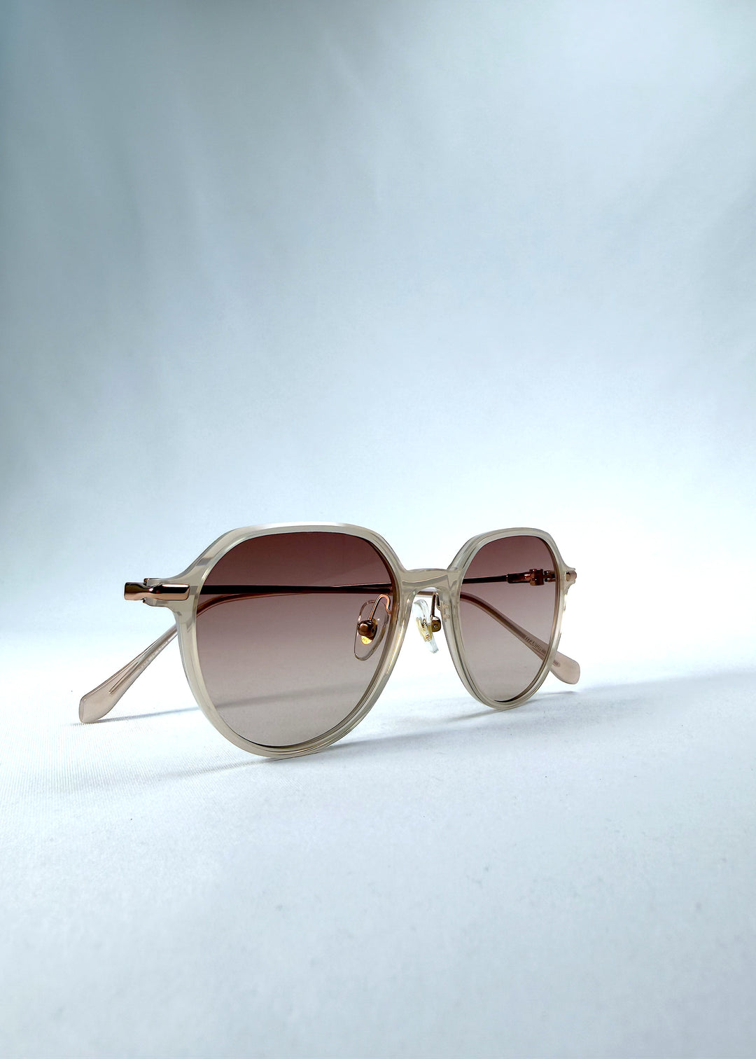 Folded view of AZE Vireo Arc sunglasses in Roselight, featuring a translucent ivory frame and soft rose gradient lenses, showing the folded temples and frame profile.