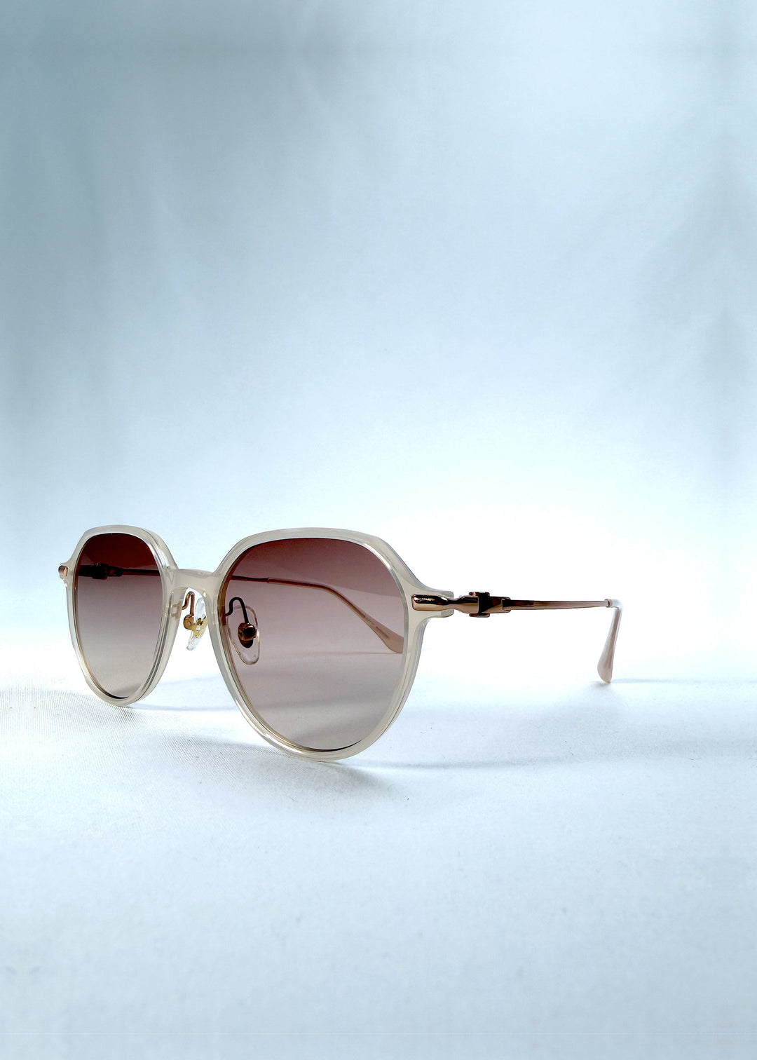 Three-quarter front view of AZE Vireo Arc sunglasses in Roselight, featuring a translucent ivory frame and soft rose gradient lenses, showing the frame shape and temple profile. 
