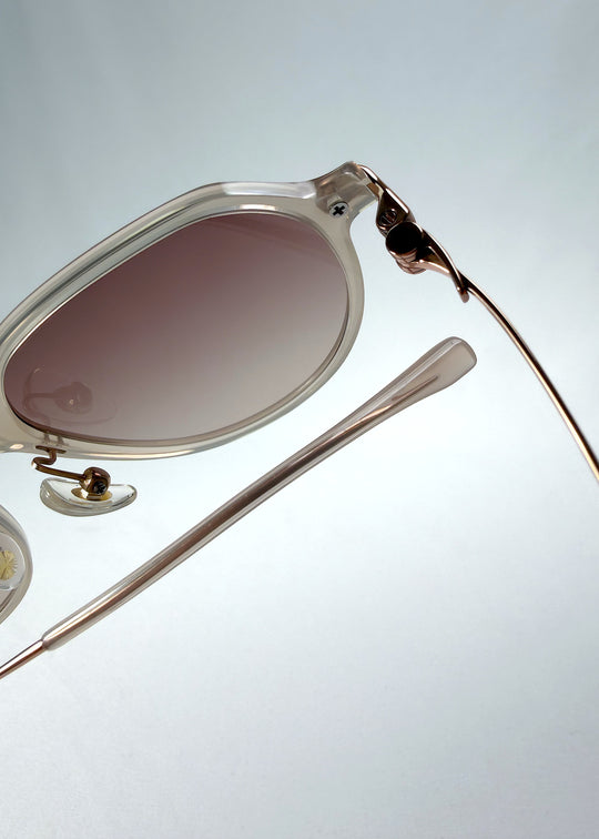 Close-up hinge detail view of AZE Vireo Arc sunglasses in Roselight, featuring a translucent ivory frame and soft rose gradient lenses, showing the hinge construction, lens edge, and temple connection.