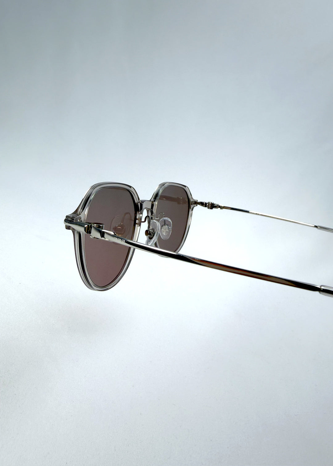 Close-up hinge detail view of AZE Vireo Arc sunglasses in Taupe Rosé, featuring a translucent taupe frame and rose-brown gradient lenses, showing the hinge construction, lens edge, and temple connection.