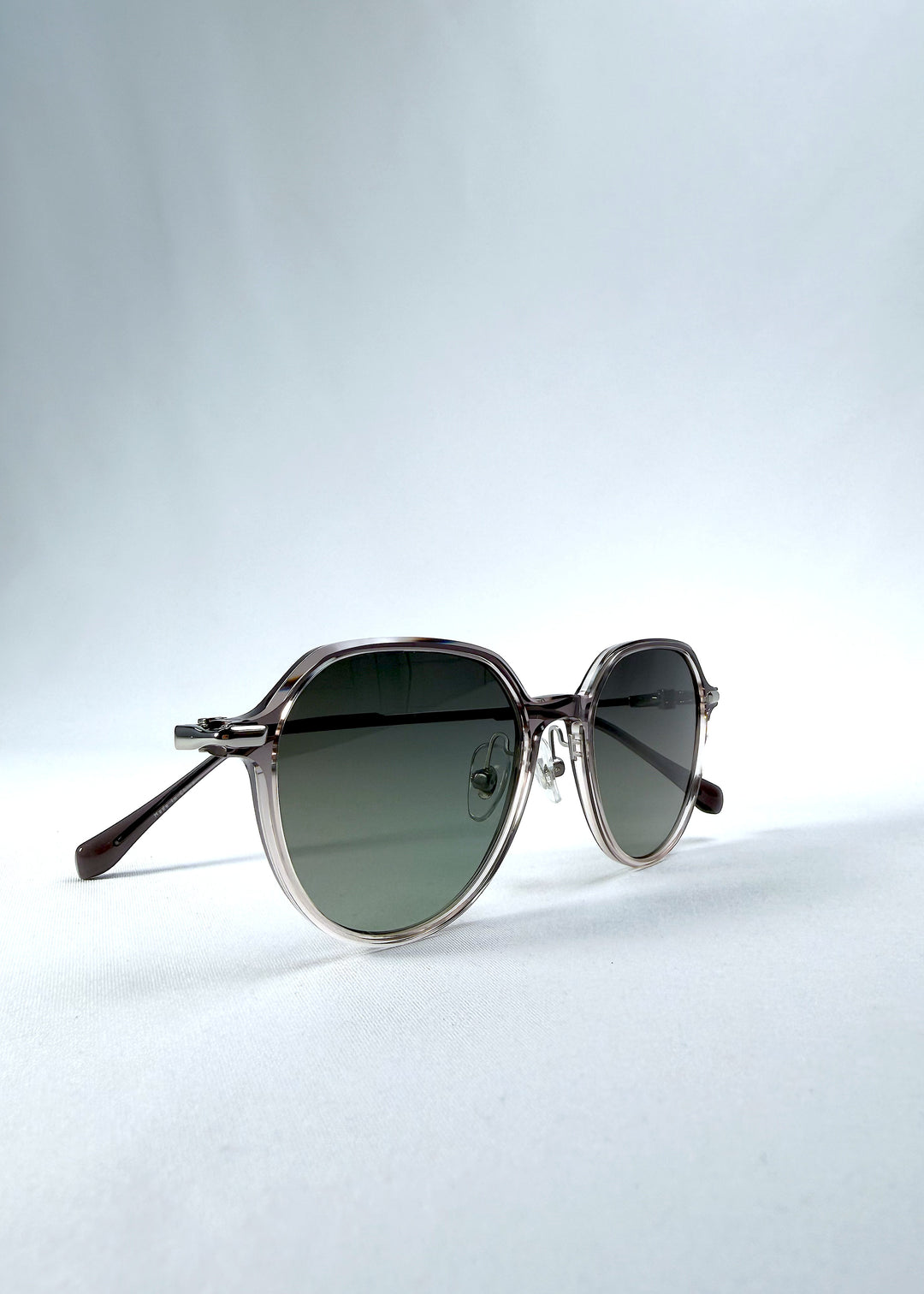Folded view of AZE Vireo Arc sunglasses in Verdant Halo, featuring a translucent smoky mauve frame and green gradient lenses, showing the folded temples and frame profile.