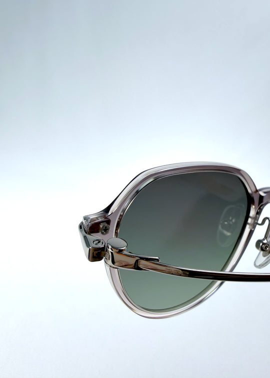 Close-up hinge detail view of AZE Vireo Arc sunglasses in Verdant Halo, featuring a translucent smoky mauve frame and green gradient lenses, showing the hinge construction, lens edge, and temple connection.